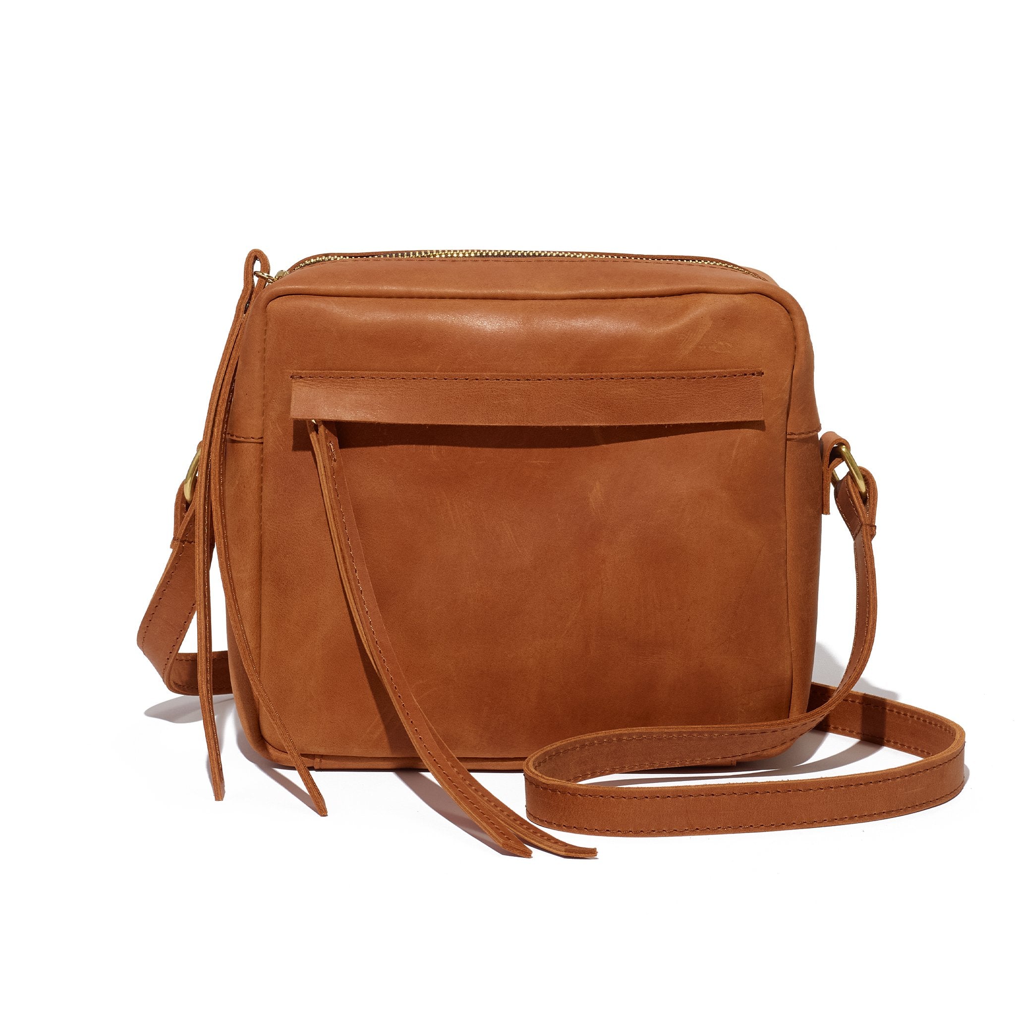 A brown crossbody camera bag handcrafted from sustainable leather and upcycled brass hardware, featuring a hand-loomed cotton lining and an interior pocket.